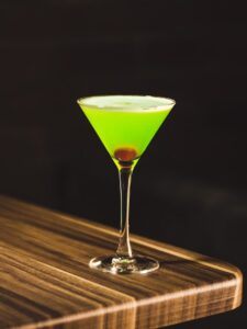 green drink in wine glass on corner of wooden table