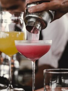 person holding cocktail shaker pouring liquid in glass during daytime
